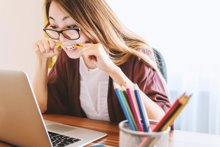 woman biting pencil while sitting on chair in front of computer during daytime photo – Free People Image on Unsplash
